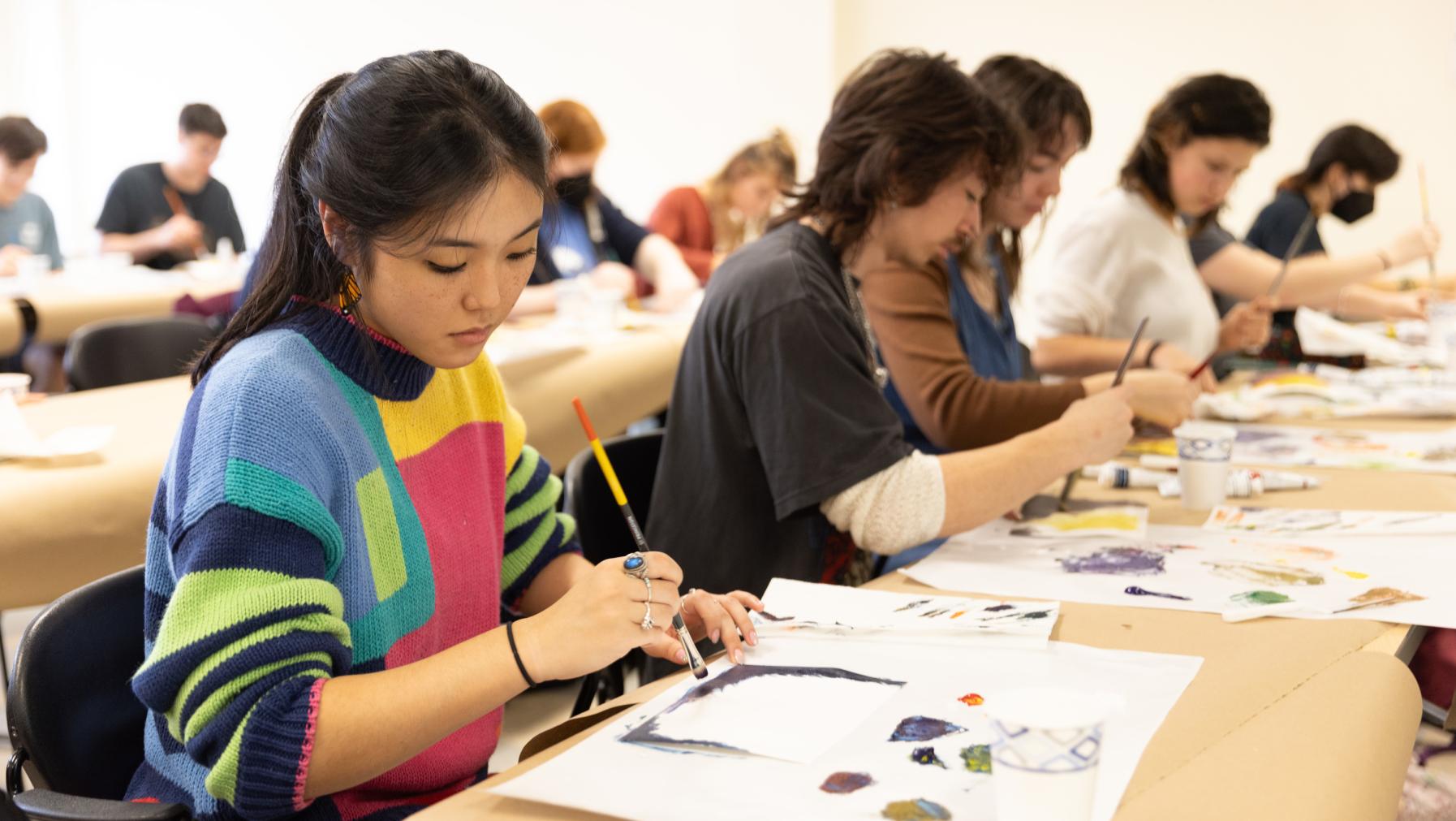 A student in a colorful sweater paints during a studio session.
