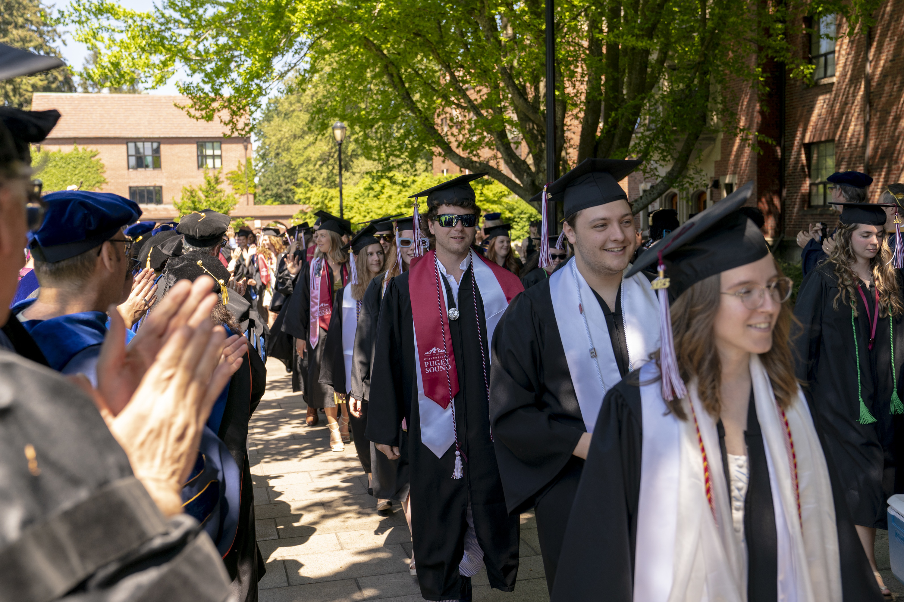 A line of students in graduation regalia walk toward the camera. 