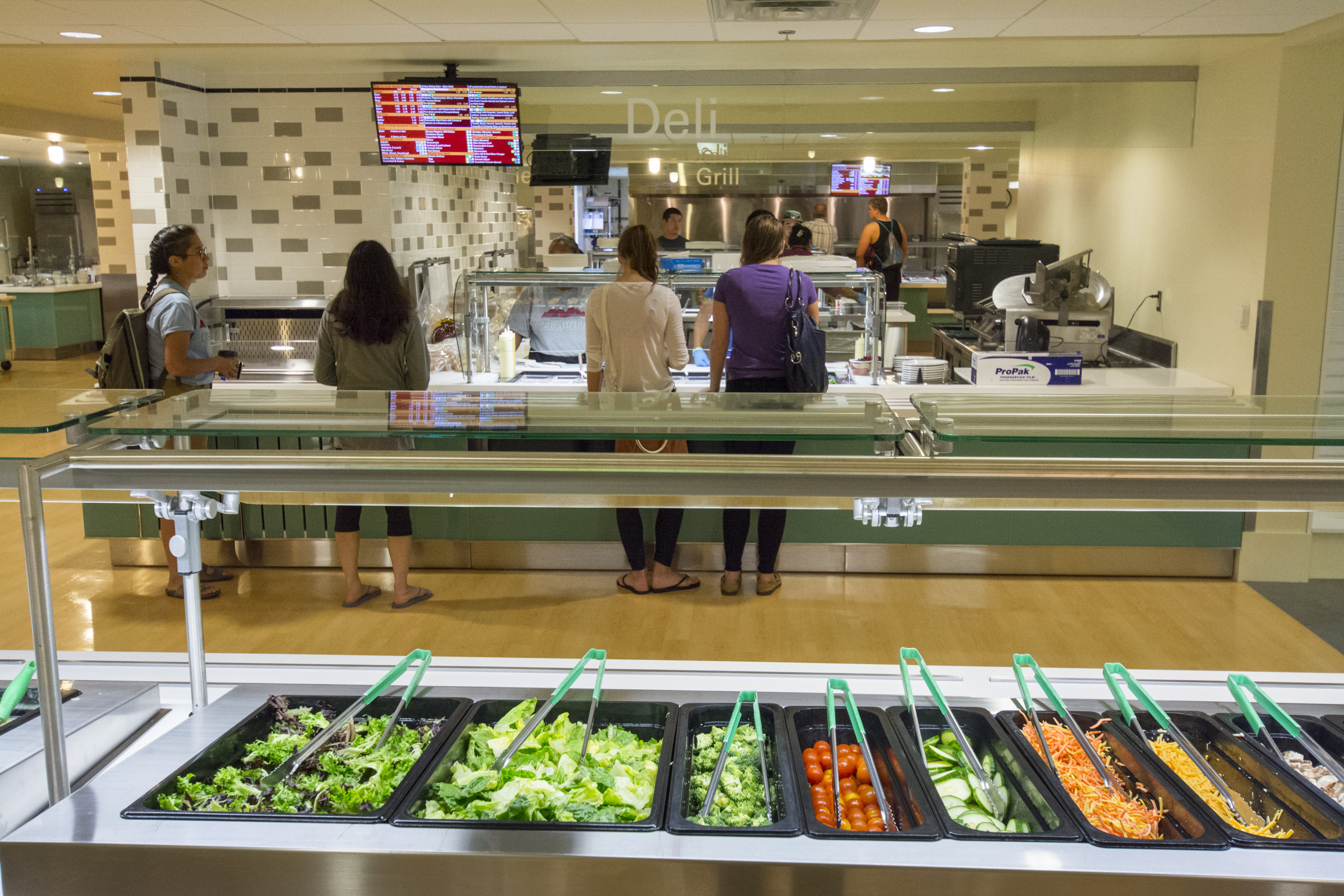 A salad bar with lettuce, tomatoes, cucumbers, and cheese. 