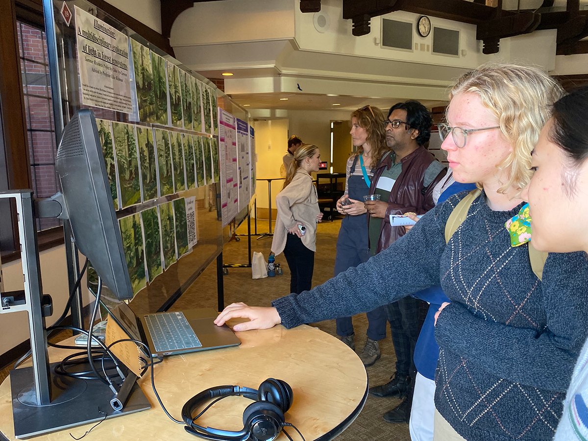 Students and faculty examine Chloe Ivy-Curwen's project at the Summer Research Symposium, 2024