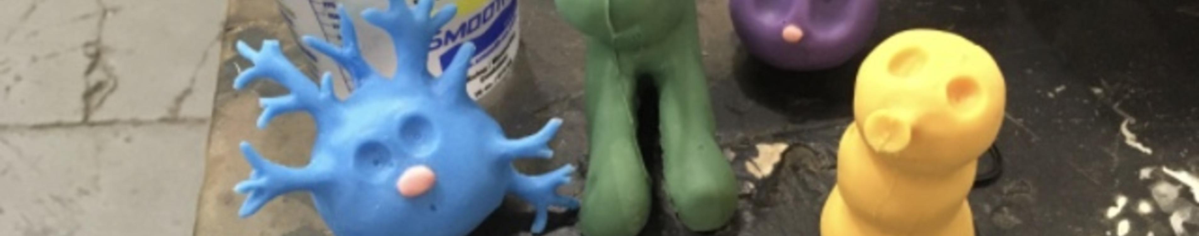 Blue, green, purple, and yellow claymation figures sit on the corner of a work table