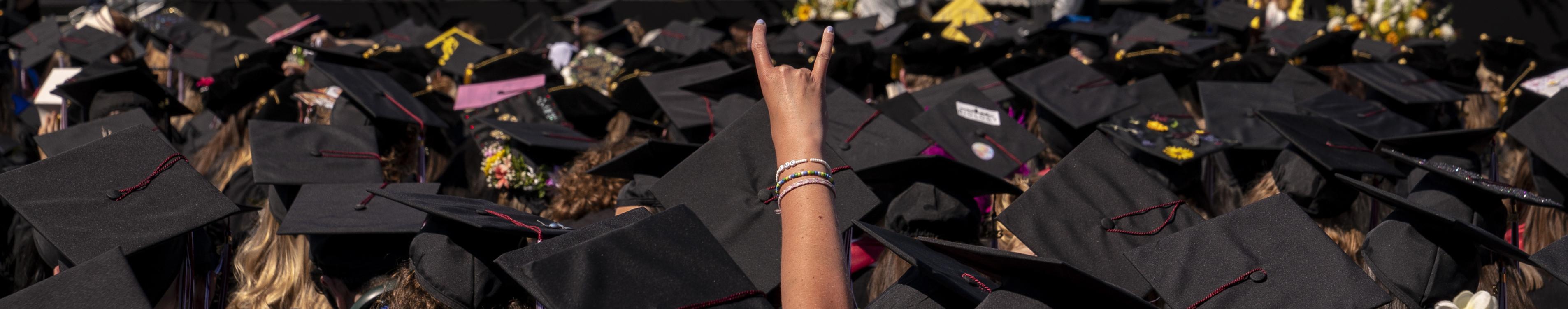 An arms shoots out above a dozen black mortar boards at a graduation ceremony. 