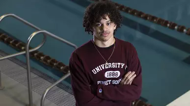 Jaden Francis ’25 stands in the Athletics and Aquatics Center, with the pool immediately behind him