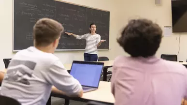 Prof. Courtney Thatcher stands at the chalkboard during a class