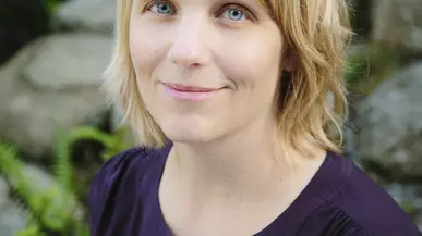 Tanya Erzen is smiling facing the camera in a purple blouse. 