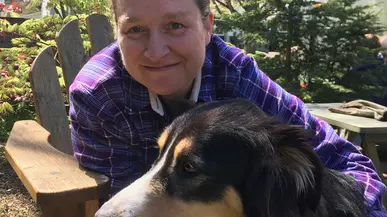 Kristin Johnson hugs her black, brown and white dog while sitting in a chair. 