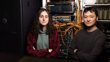 Julia and Prof. Chiu stand in front of computer equipment with wiring falling behind them. 