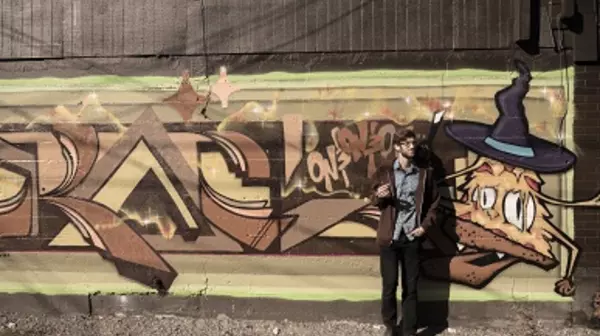 A student stands in front of a colorful mural on 6th Ave.