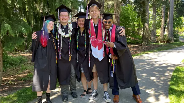 Five students in graduation gowns stand together smiling.