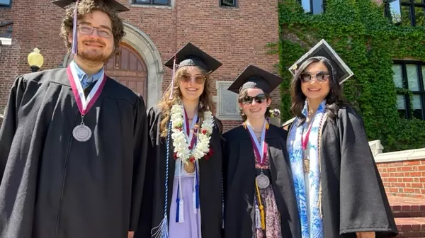 Four students standing together in graduation gowns.