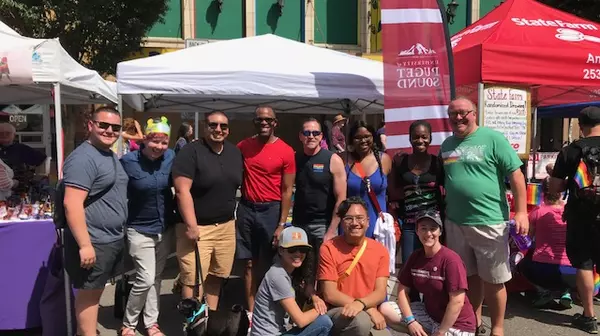 Roughly 10 people gather in front of a canopied booth on the street and pose, smiling at the camera.