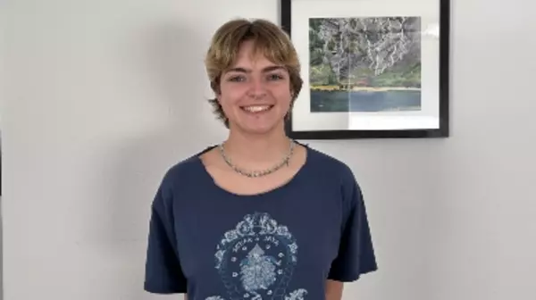 Alex standing in front of a white wall with a framed piece of art