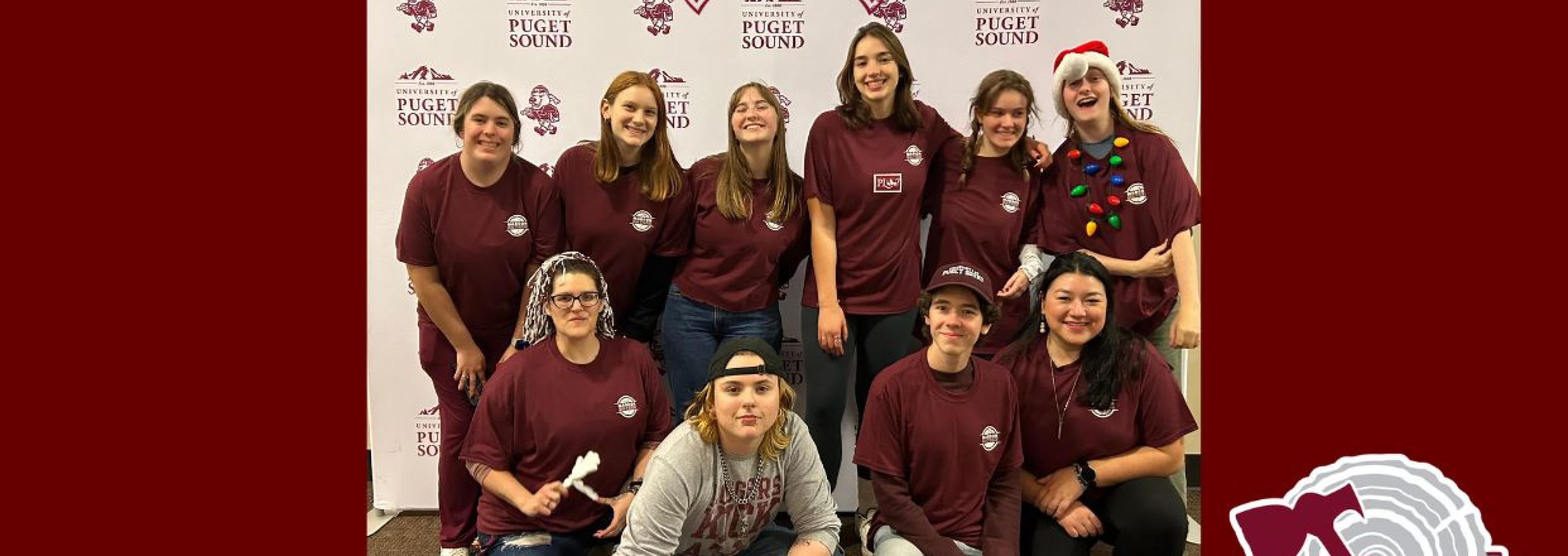Group photo of Maroon Society members at a Maroon Mayhem event standing in front of a University of Puget Sound background