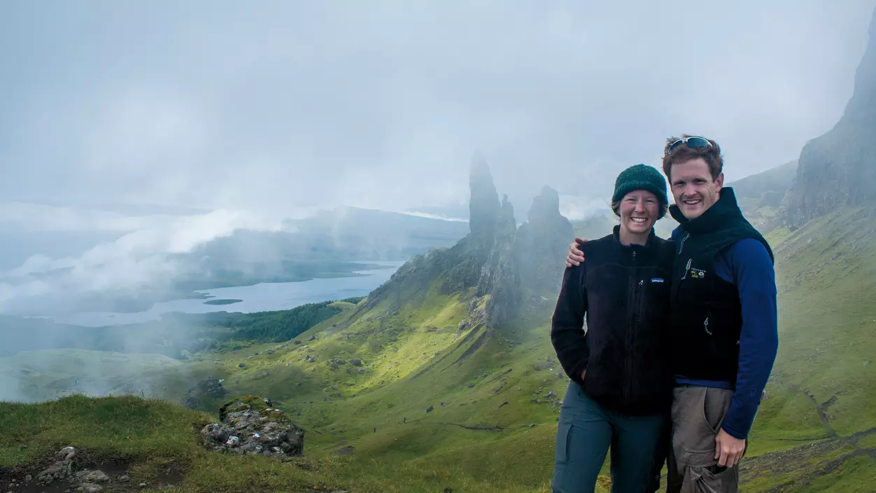 Two people standing outside with a hilly landscape in the distance