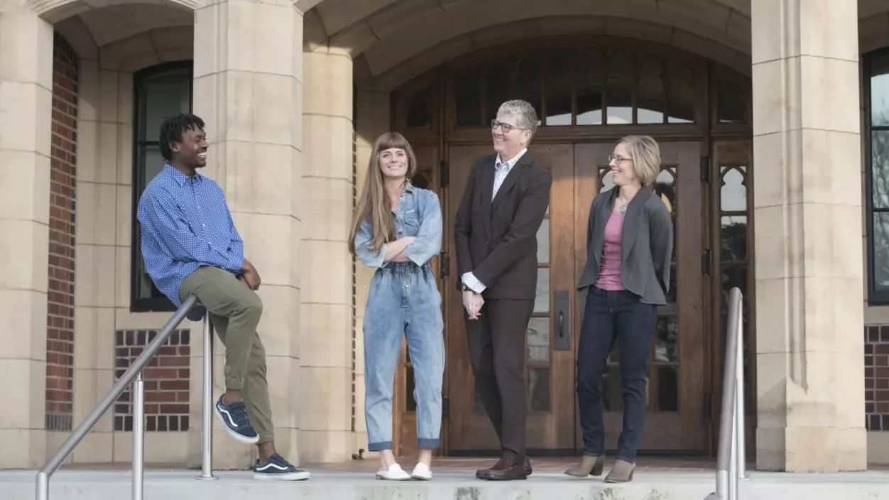 Four people smiling in front of the entrance of a school