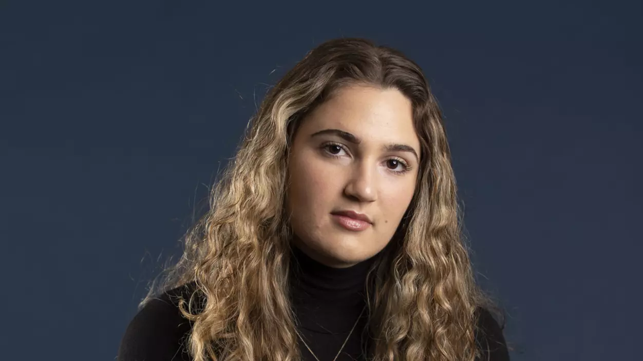 A person seated on a stool and posing for the camera