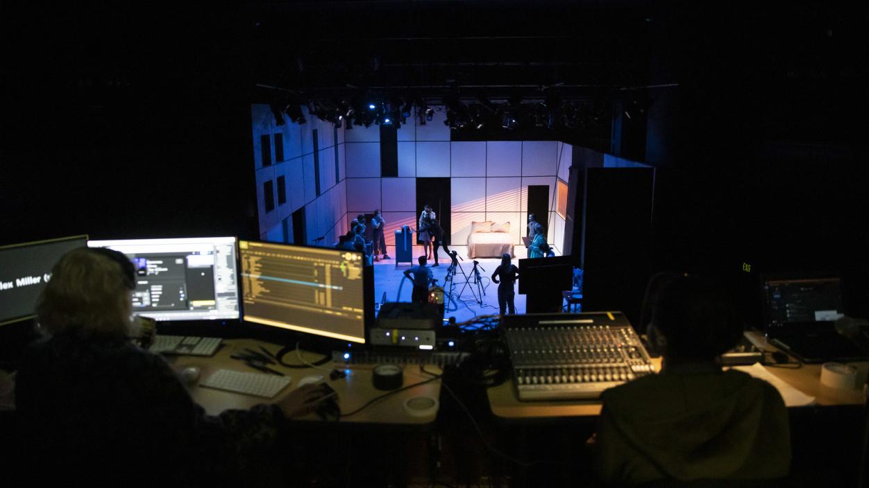 Students sit in a dimly lit control room above the Norton Clapp Theatre stage, preparing for a dress rehearsal of Machinal in March 2021