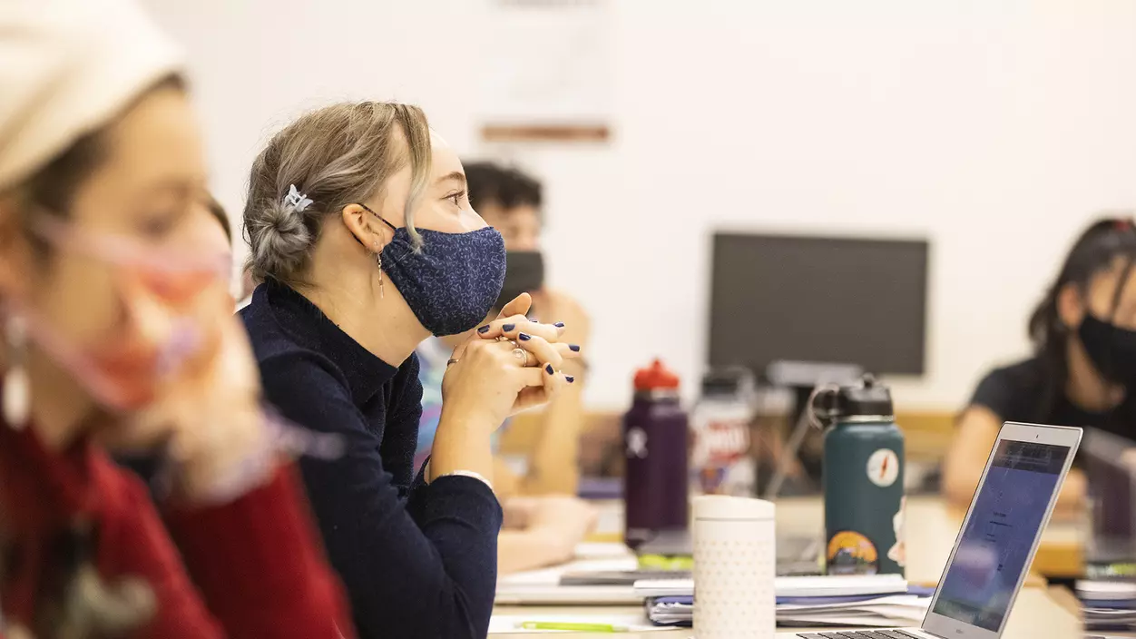 A masked female student listens attentively during class