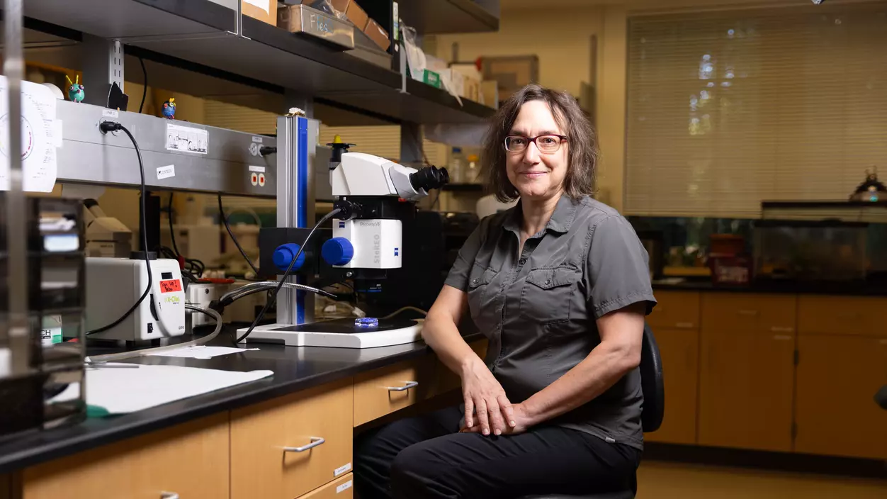 Professor of Biology Leslie Saucedo sits beside a microscope in her lab.