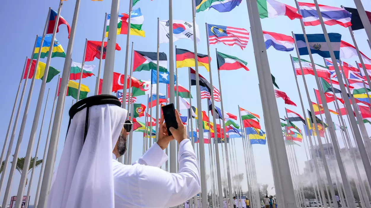 A figure dressed in white takes a photo of an array of national flags with a smartphone.