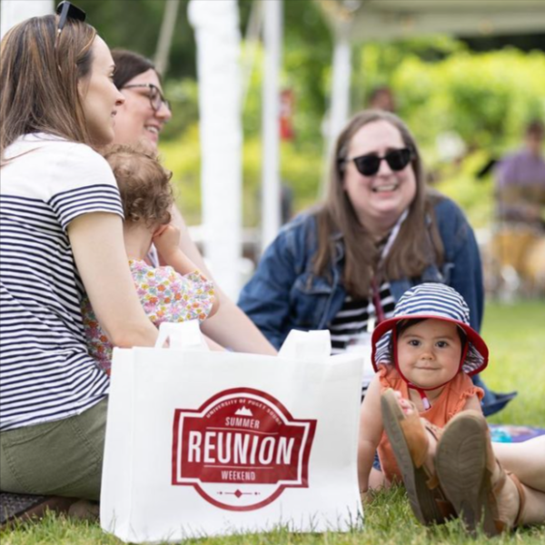 Attendees at Summer Reunion Weekend relax on the grassy Event Lawn during a barbecue--including an adorable future Logger!