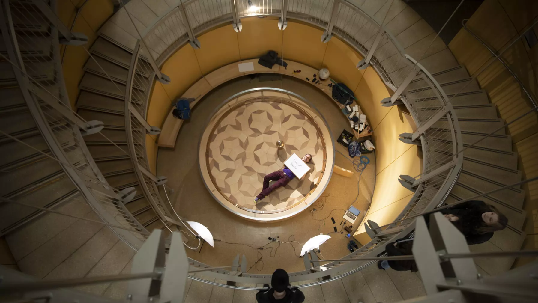 Kurtis Baute lies on the platform of the Foucault pendulum in Harned Hall