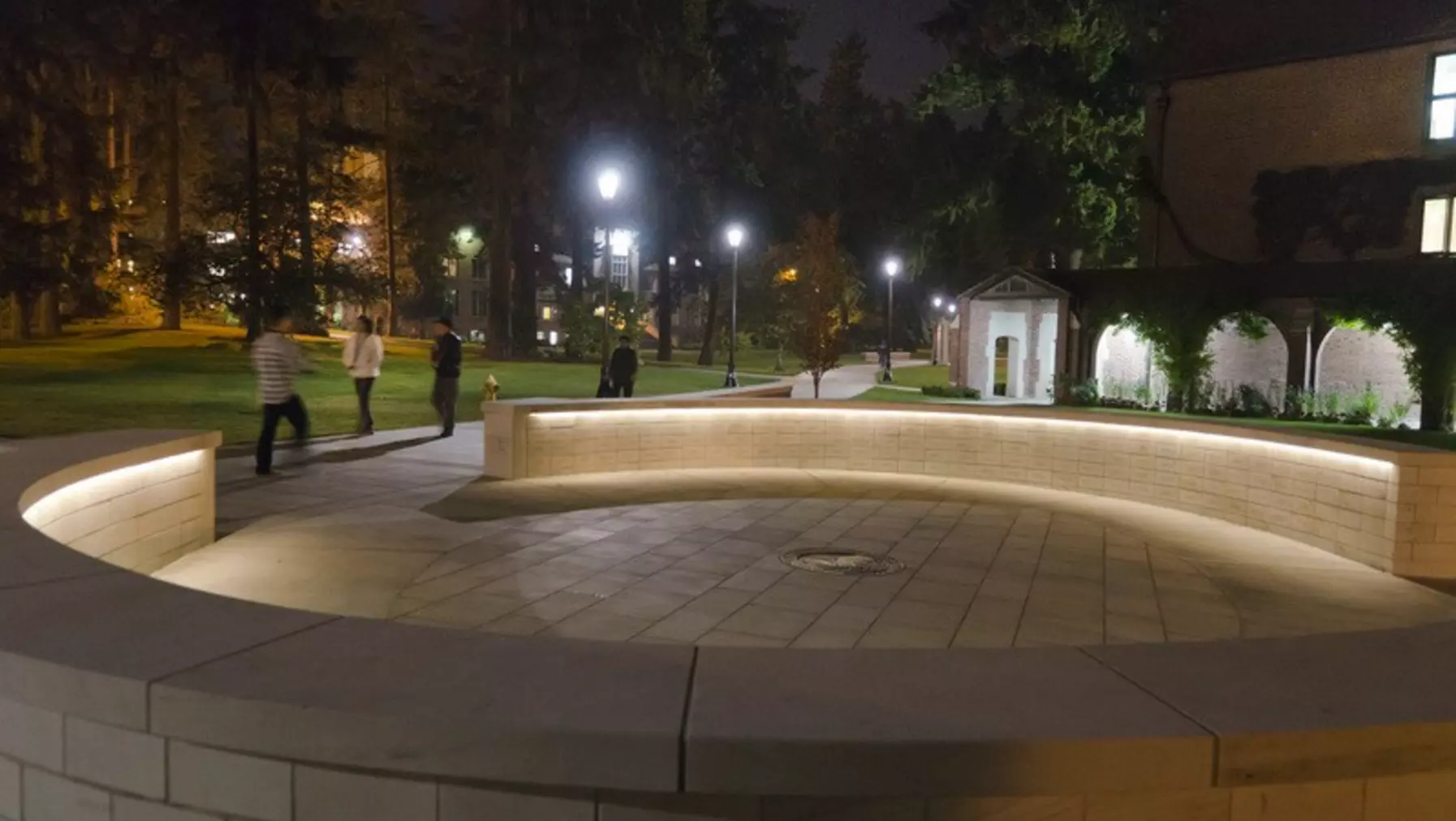 Benefactor Plaza illuminated in the evening with people walking by