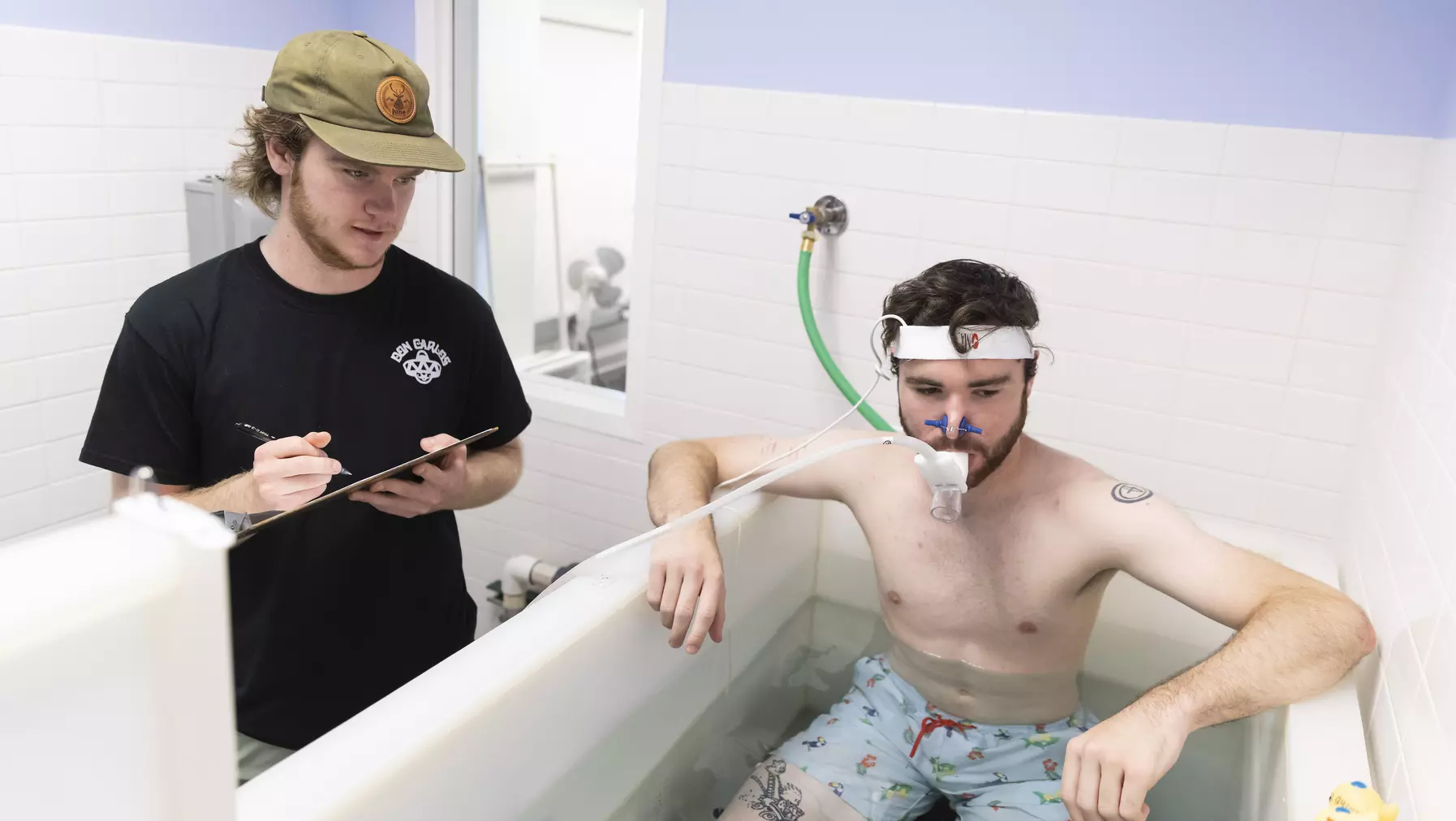 Chris Nicol ’24 monitors Graham Hall ’24 as he sits in a tub of water while hooked up to monitoring equipment.