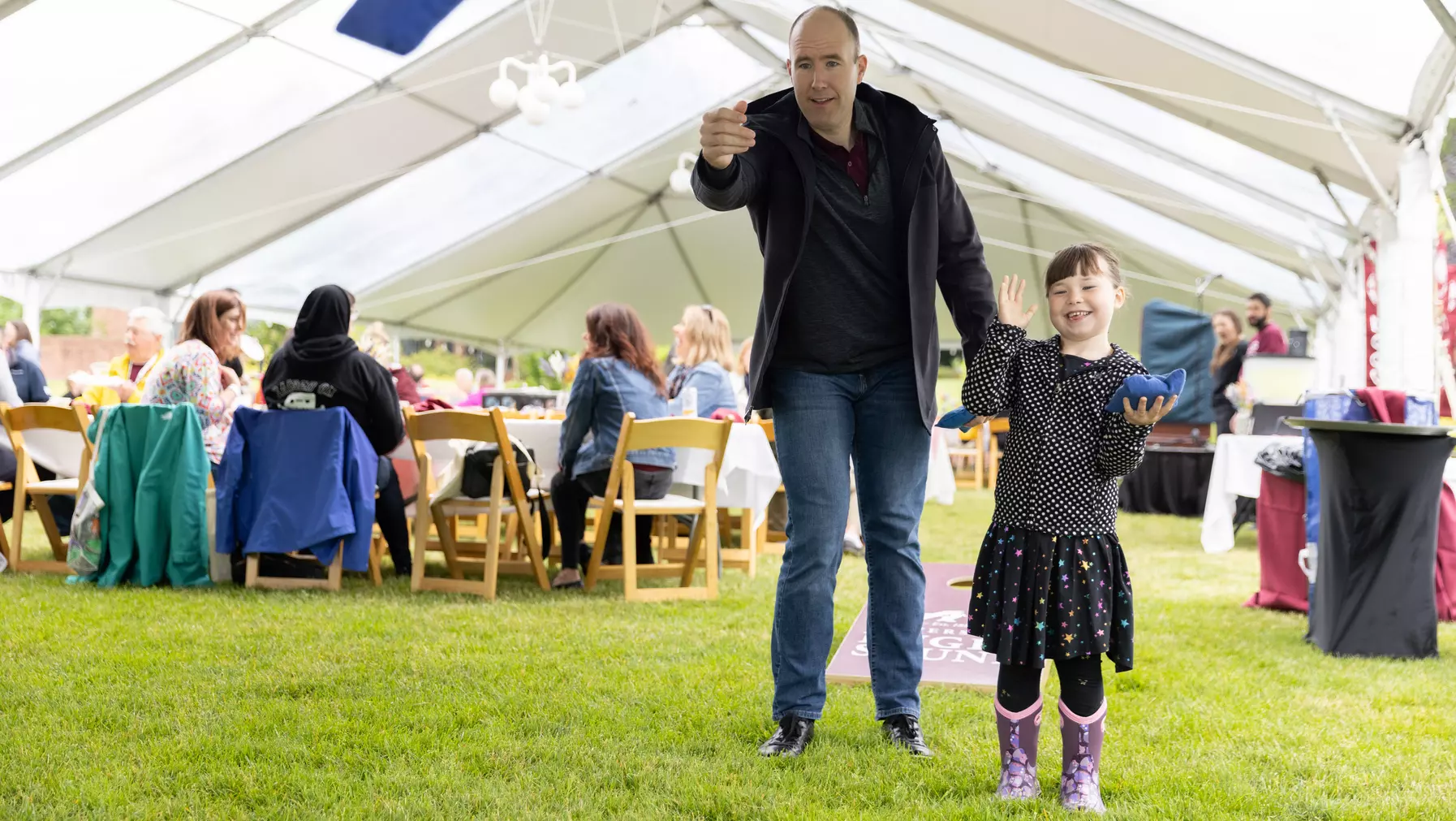 A family plays bean bag toss at Summer Reunion Weekend 2023.