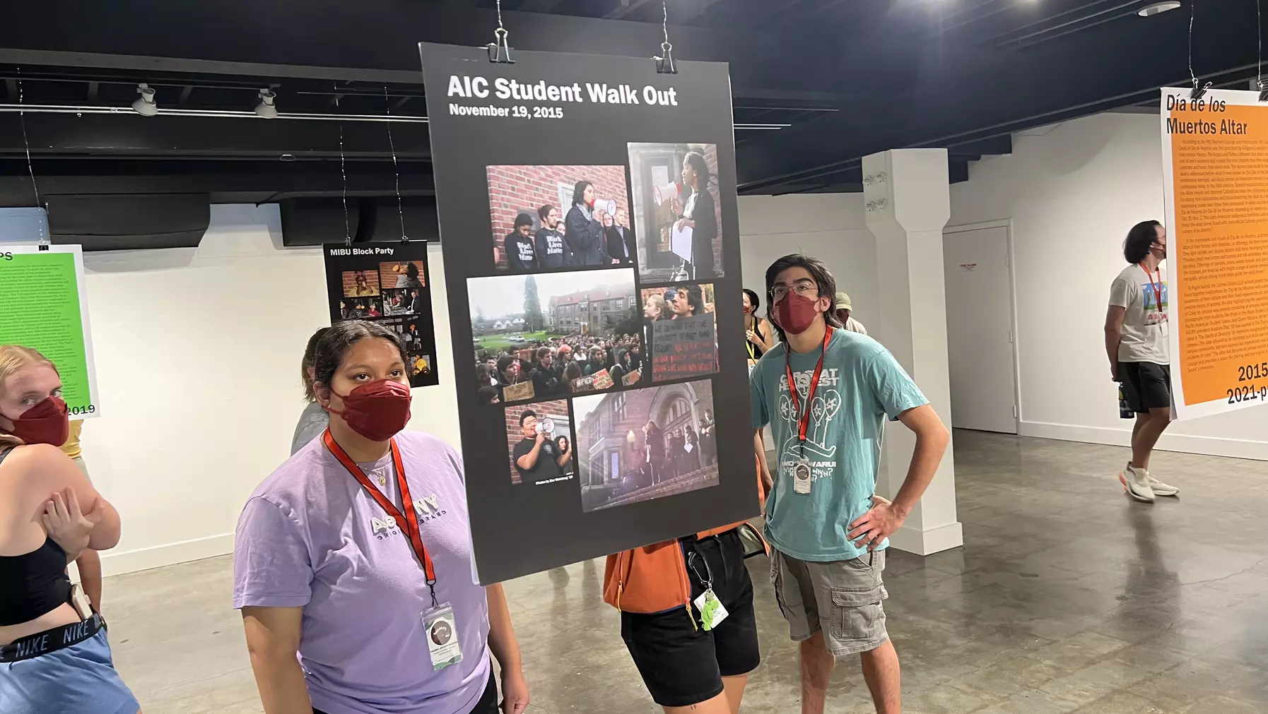 Two students wearing masks stand reading a sign that hangs from the ceiling.