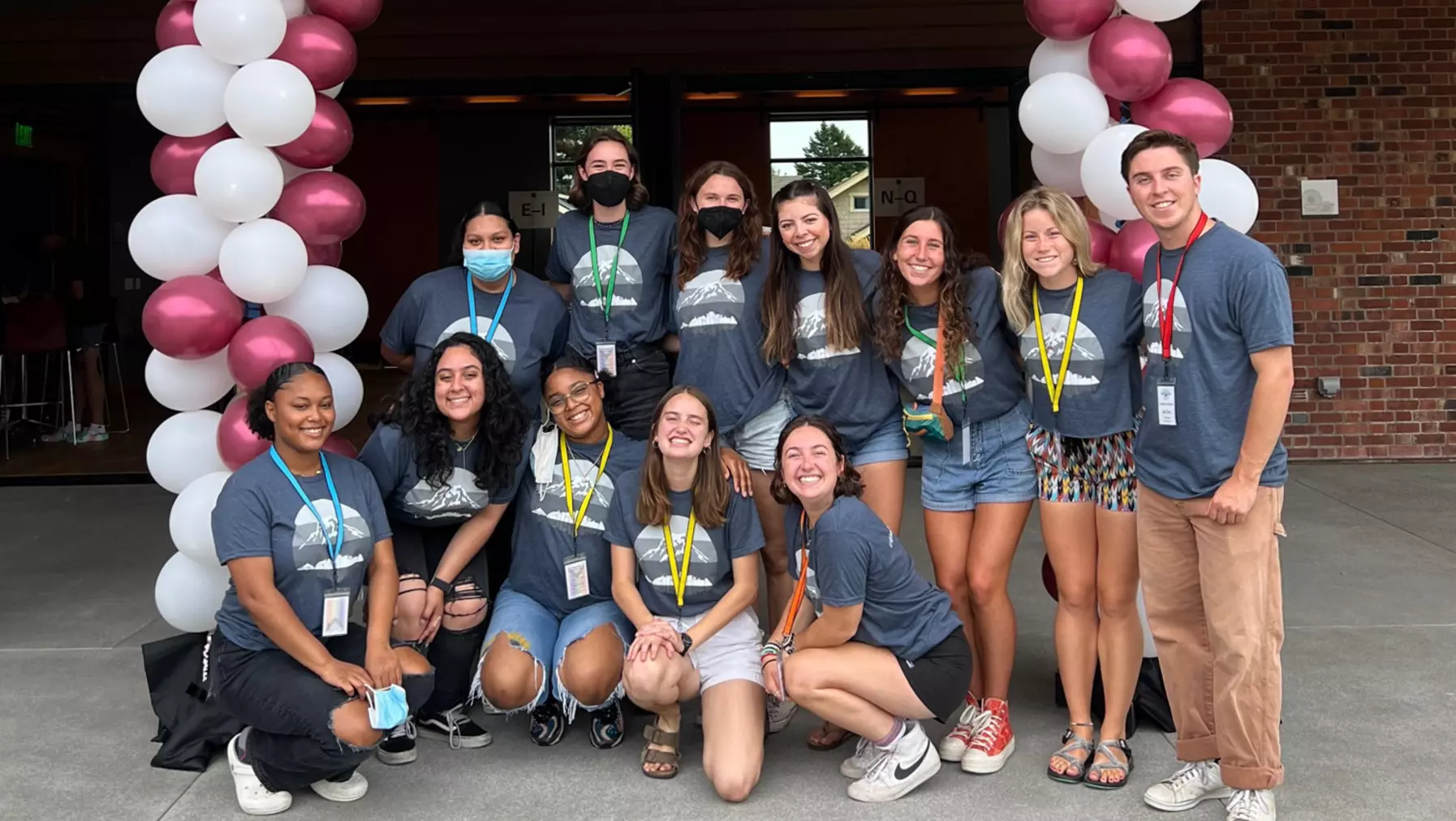 A group of students stand under a balloon arch and smile.