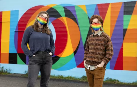 Two people standing in front of a colorful mural