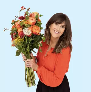 Jennifer Cramer-Miller ’87 holds a bouquet of flowers in front of a blue background and looks at the camera.