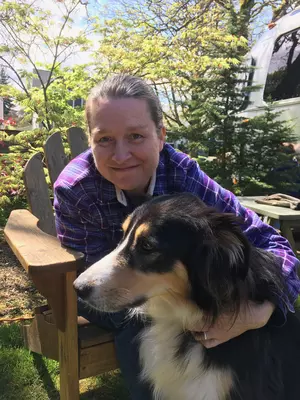 Kristin Johnson hugs her black, brown and white dog while sitting in a chair. 