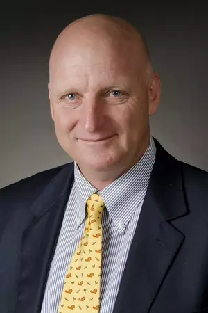 A man in a black suit jacket and yellow tie. 